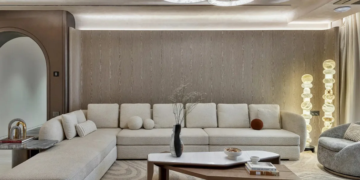 Modern luxury living room by Sumessh Menon Associates featuring a curved cream sectional sofa, minimalist marble coffee table, and textured wood-panelled accent wall.